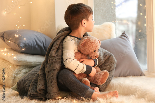 Cute little boy with teddy bear near window at home photo