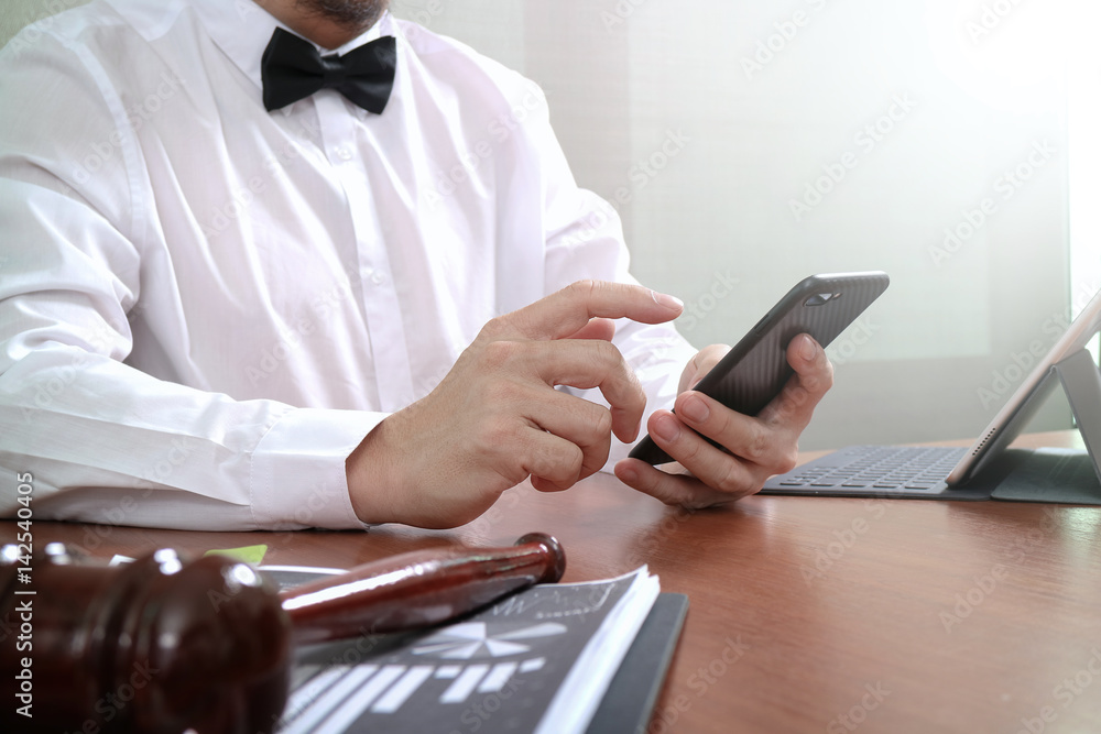 Fototapeta premium Justice and Law context.Male lawyer hand working with smart phone,digital tablet computer docking keyboard with gavel and document on wood table