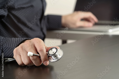 close up of smart medical doctor working with stethoscope and laptop computer on dark wooden desk