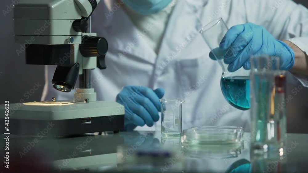 Lab assistant pouring needed reagent into beaker to create chemical solution Lab assistant pouring needed reagent into beaker to create chemical solution