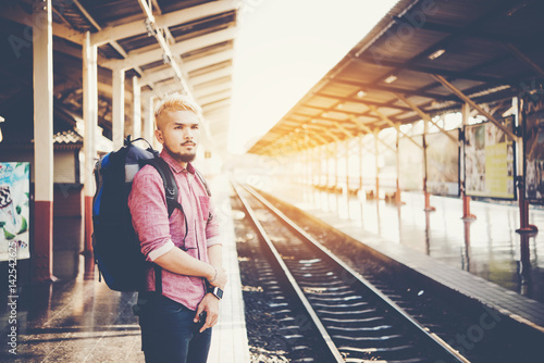 Young hipster man walking in platform looking away while waiting for the train at the railway station. Travel concept.