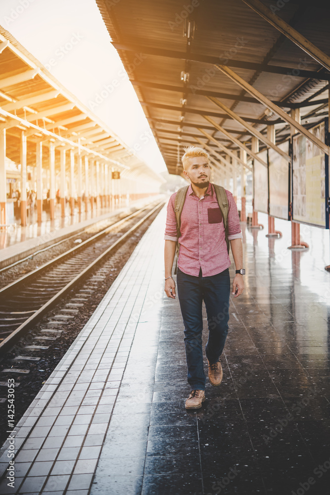 Young hipster man walking in platform looking away while waiting for the train at the railway station. Travel concept.