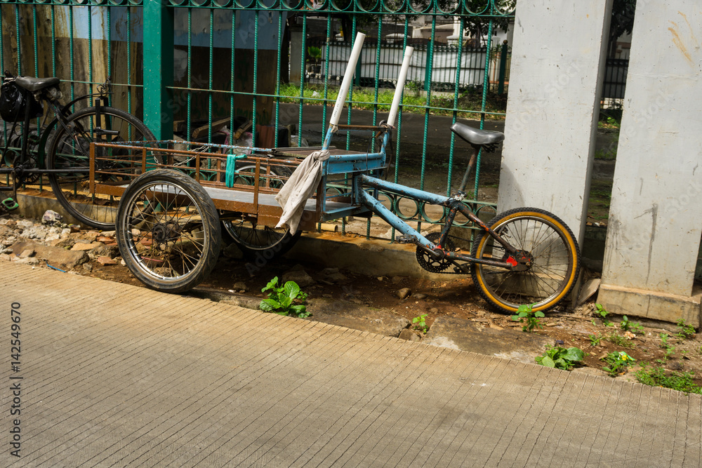 a unique transportation combination from cart and bicycle parked near green fence on side the street photo taken in Jakarta Indonesia