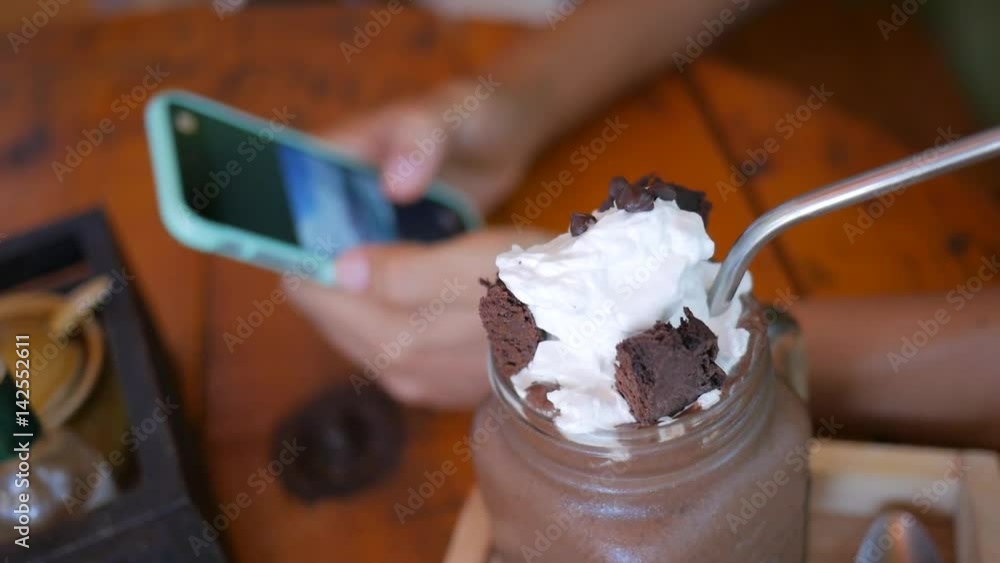 Sweet Chocolate Dessert with Cream and Young Woman Looking Pictures on Smartphone in Cafe on Background. Sweet Chocolate Dessert with Cream and Young Woman Looking Pictures on Smartphone in Cafe on Background.