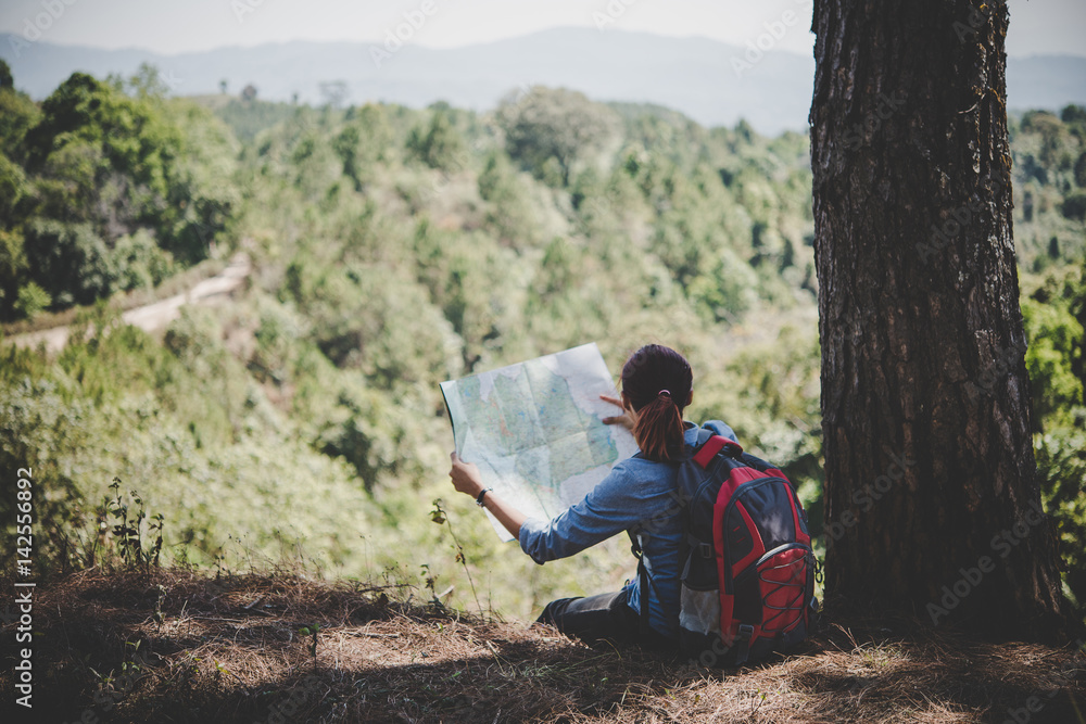 Young woman backpacker hiker reading map hiking trip looking away to find place to go. Adventure holiday.