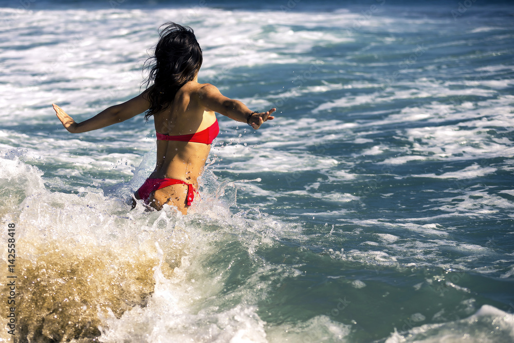 Young and attractive woman is swimming in big waves. She is running in water with raised hands up, Barcelona, Spain
