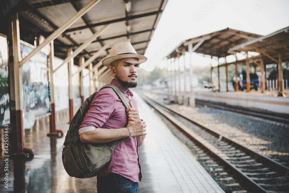 Young hipster man walking through train station. Man waiting for the train at platform. Travel concept.