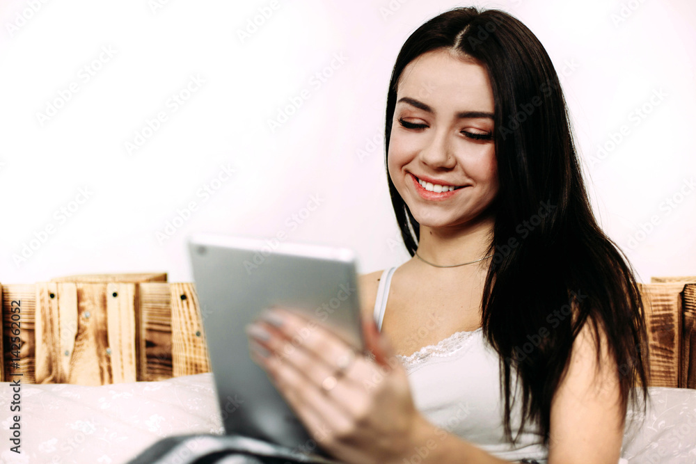 Stunning brunette lady reads something in the iPad lying on wooden bed Stunning brunette lady reads something in the iPad lying on wooden bed