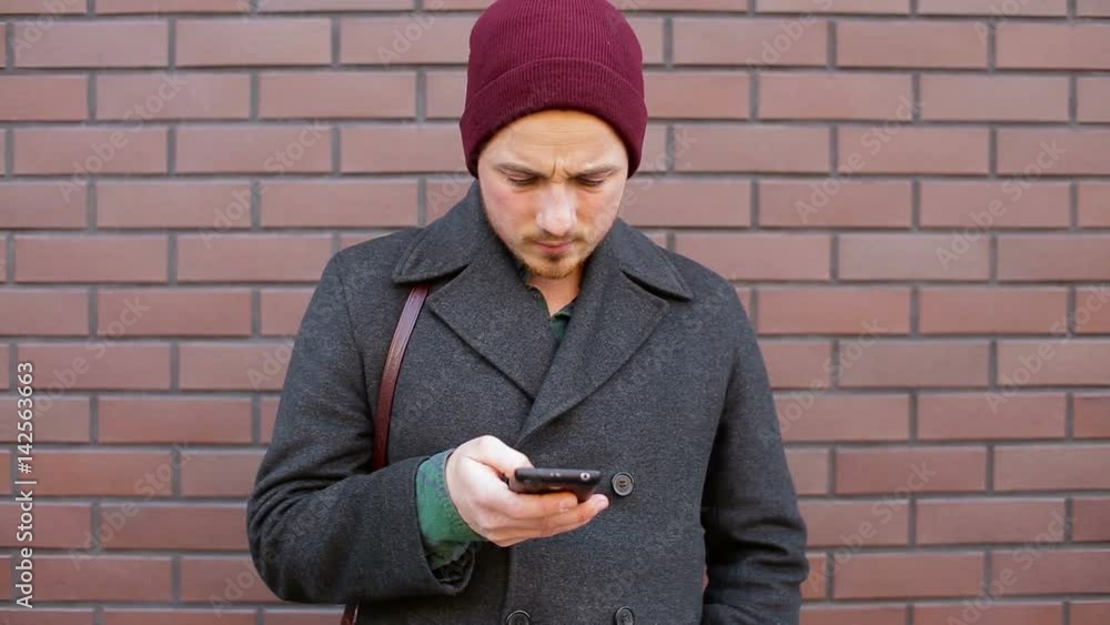 Young man using smartphone standing by brick wall in city Young man using smartphone standing by brick wall in city