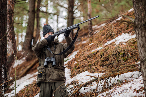 male hunter ready to hunt, holding gun and walking in forest.