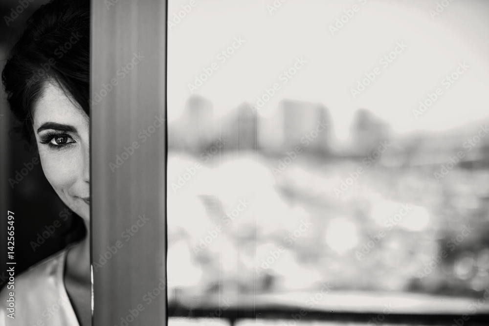 Brunette woman looks from behind the balcony door Brunette woman looks from behind the balcony door
