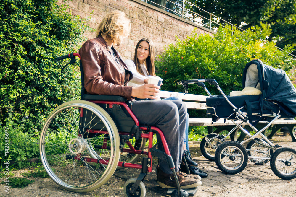 Young Parents In Wheelchair With Baby Stroller In The Park Young Parents In Wheelchair With Baby Stroller In The Park