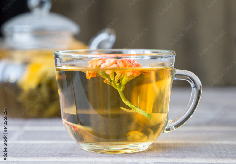 Closeup of cup of tea with bright flower on wooden table with teapot on background. still life with tea cup. Closeup of cup of tea with bright flower on wooden table with teapot on background. still life with tea cup.