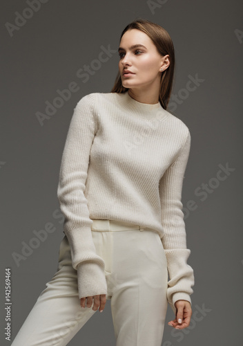 Fashion style model in white sweater and pants, posing in the studio