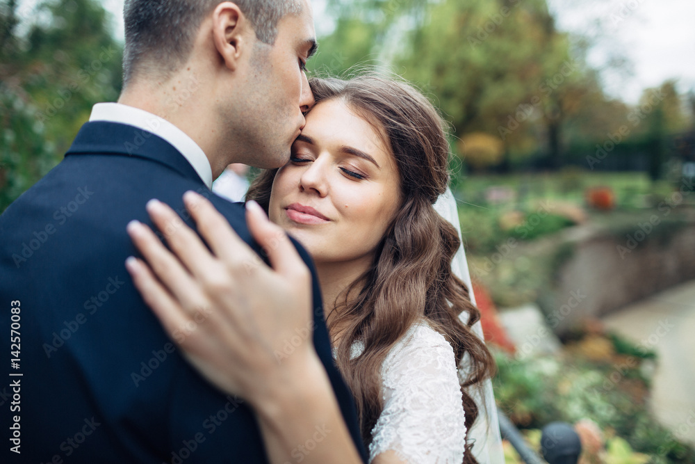 Groom kisses bride's forehead tender while she leans to him Groom kisses bride's forehead tender while she leans to him
