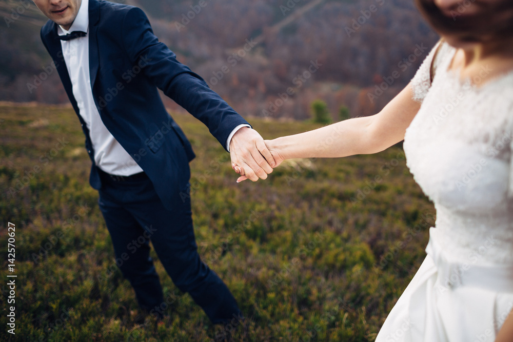 Close-up of newlyweds hands held tightly together while they stand on windy hill Close-up of newlyweds hands held tightly together while they stand on windy hill
