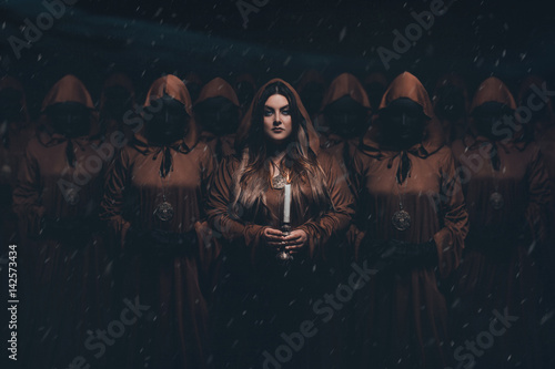 A girl servant wanders around with candles. A crowd of people in masks wearing robes. Creative colors photo