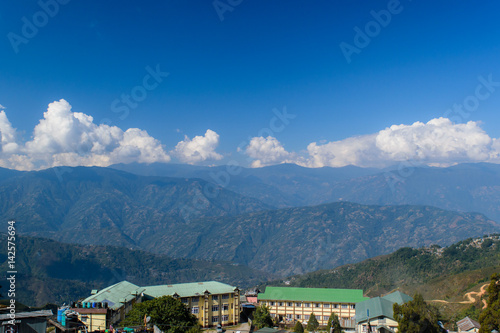 A hilltop view of house' roof with mountains and blue sky with clouds from Darjeeling Himalayan railway station on a misty morning. © ABIR