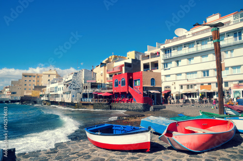 Beautiful view of El Medano, little town in the south of Tenerife. Red wooden fishing boats on the beach and coastal promenade in El Medano village. Tenerife, Canary islands, Spain.