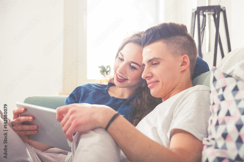 Couple on sofa at home using digital tablet and smiling Couple on sofa at home using digital tablet and smiling