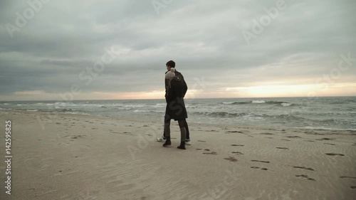 Young couple looking at the sea, walking the beach, coat and hat, Baltic or Iceland cold weather