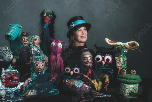 Smiling puppeteer standing between handmade puppets.