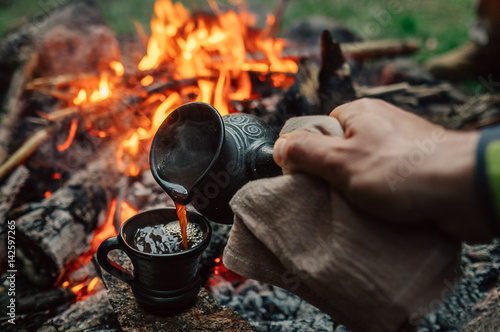 Making coffee process on the campfire. Man pour coffe in potter cup