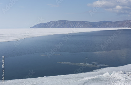 Baikal lake spring landscape view. Snow-covered shore of the lake. Rocky forested coastline. Boundary of ice and open water. © anya babii