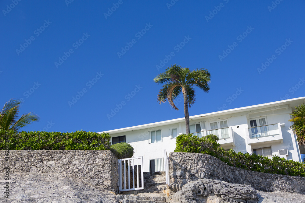 Bungalows on the beach. Palm tree on the yard. Blue sky. White gate open.
