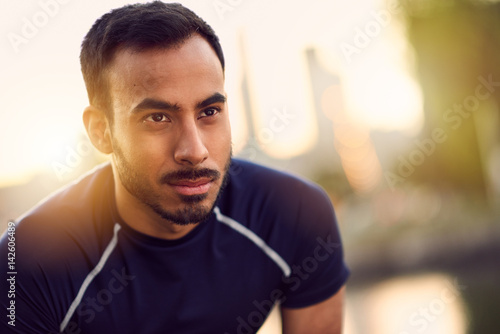 Portrait of active millenial man jogging at dusk with an urban cityscape and sunset in the background
