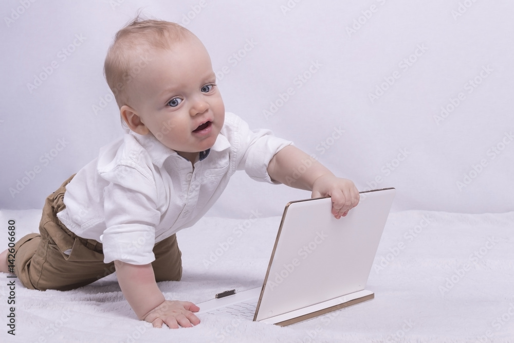 Cute thoughtful boy in white shirt playing with a tablet. Funny infant boy with laptop looks like little businessman Cute thoughtful boy in white shirt playing with a tablet. Funny infant boy with laptop looks like little businessman