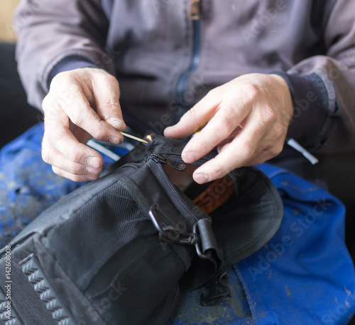 Tailor man sews up a bag in a workshop