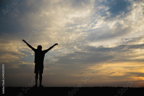 Silhouette of a man with hands raised in the sunset.