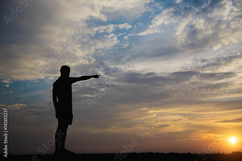 Silhouette of a man with hands point to sky in the sunset.