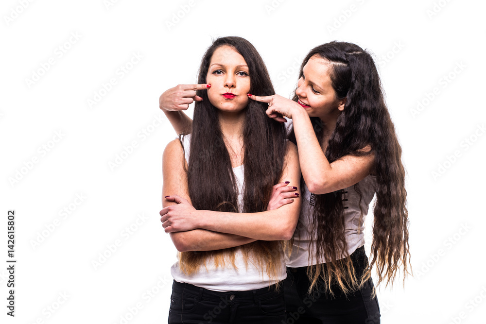 Twins sisters. One sister make sad faces other try to make funny faces on white background Twins sisters. One sister make sad faces other try to make funny faces on white background