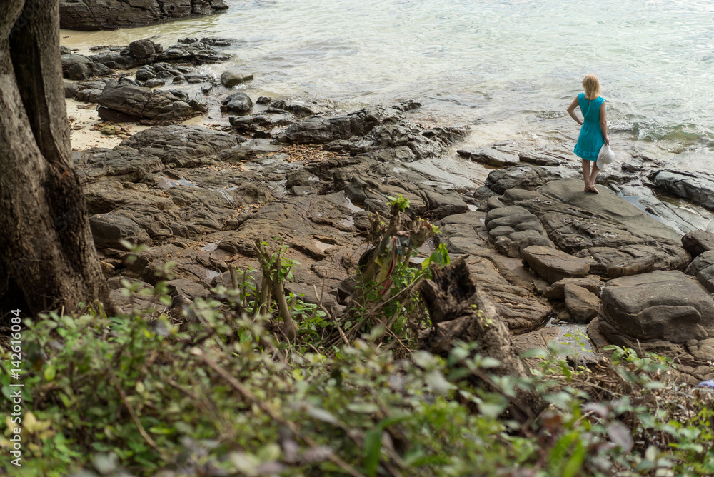 Young woman in blue dress staying on the rocky beach Young woman in blue dress staying on the rocky beach