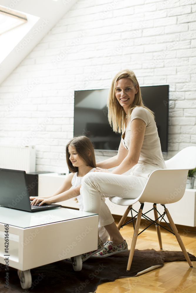 Mother and daughter using computer and sitting in the room
