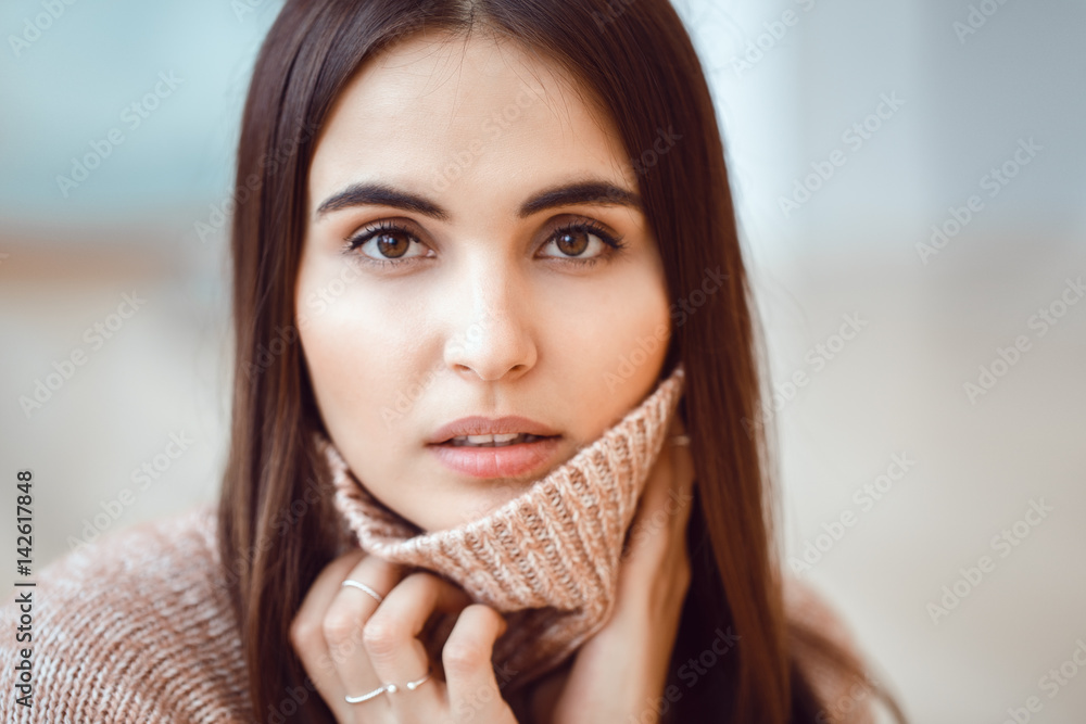 Fototapeta premium Closeup portrait of pensive white Caucasian European brunette young beautiful woman model with long dark red hair and brown eyes in turtleneck sweater, looking in camera