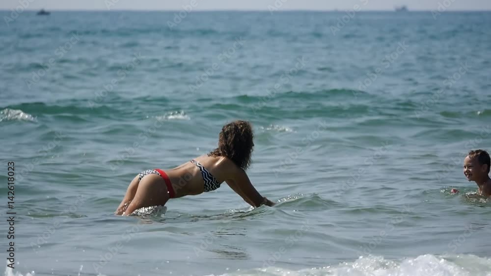 Young happy girl with child having fun playing in sea blue waves in summer vacation. Slow motion 50Fps. Young happy girl with child having fun playing in sea blue waves in summer vacation. Slow motion 50Fps.