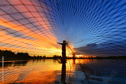 The silluate fisherman trowing the nets  on boat in river  at during sunrise,Thailand photo