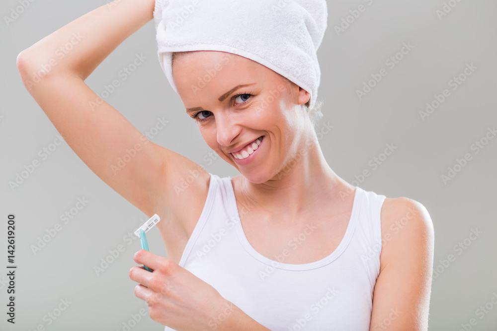 Beautiful woman is shaving under her arm on the gray background. Beautiful woman is shaving under her arm on the gray background.