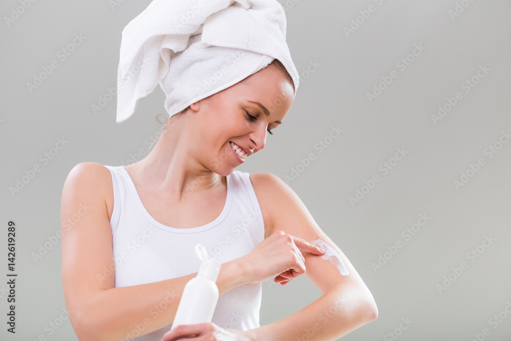 Beautiful young woman applying lotion on her arm on gray background. Beautiful young woman applying lotion on her arm on gray background.