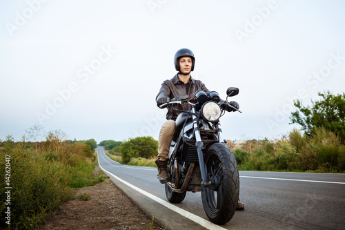 Young handsome man riding on motorbike at countryside road. © Cookie Studio