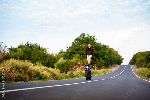 Fototapeta Naklejka Na Ścianę i Meble -  Young man riding on motorbike, doing tricks at countryside road.