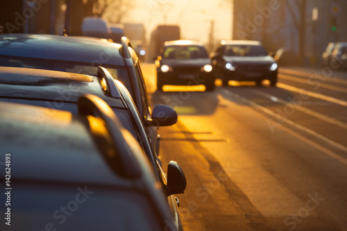 Car Overtake Street Scene / Street inside city, morning twilight with parking cars, two further blurred with illuminated headlights on the road, one pass the other (copy space)
