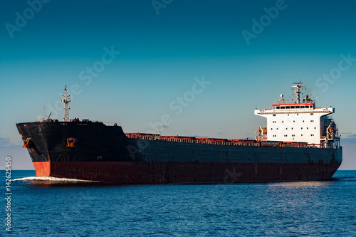 Black cargo ship moving in still Baltic sea water. Riga, Europe photo