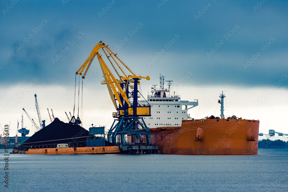 Large orange cargo ship loading with a coal in the port