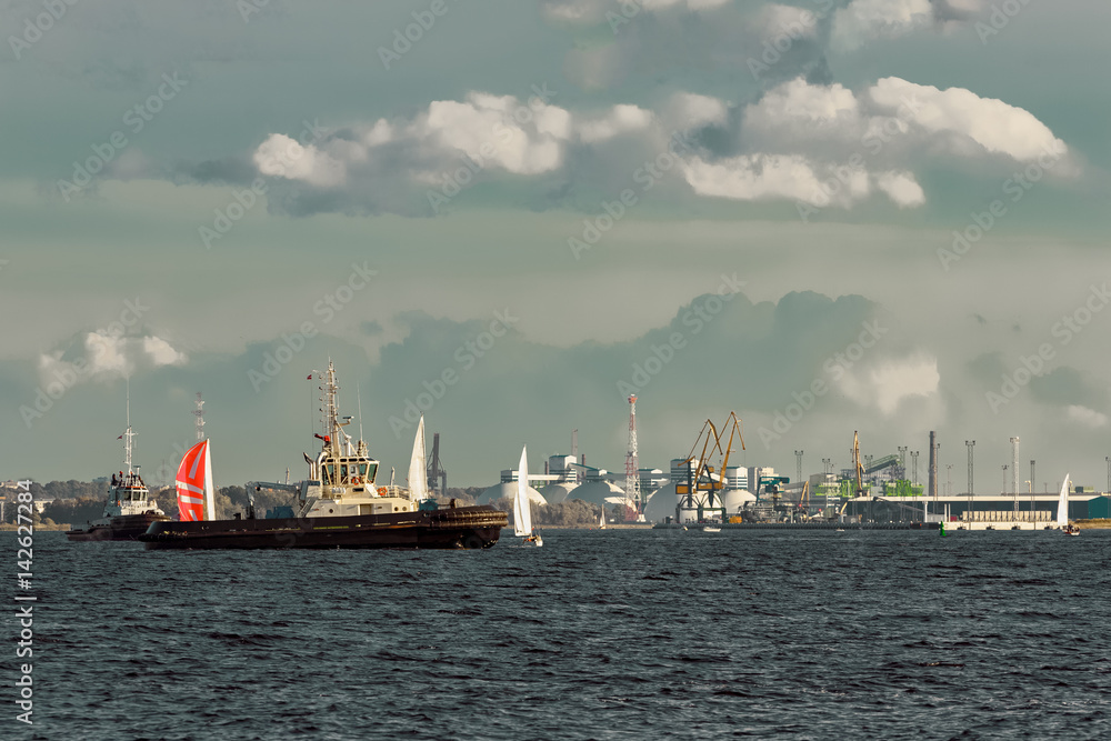 Tug ships and sailboats against cargo terminal in Riga