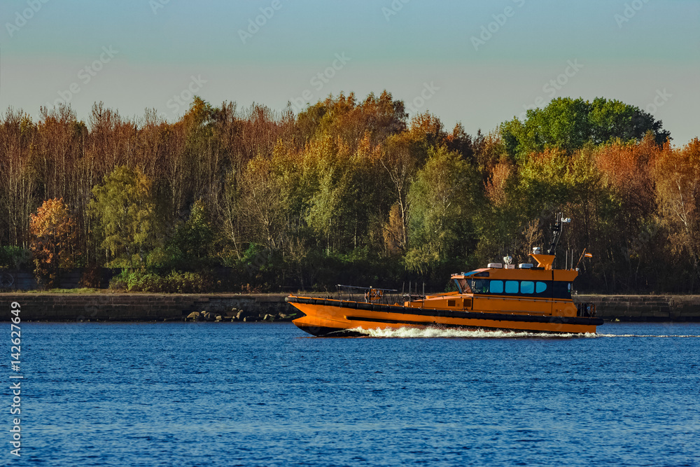 Obraz premium Orange pilot ship sailing past the autumn trees in Europe