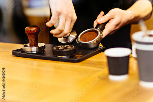 Close up of barista presses ground coffee using tamper.